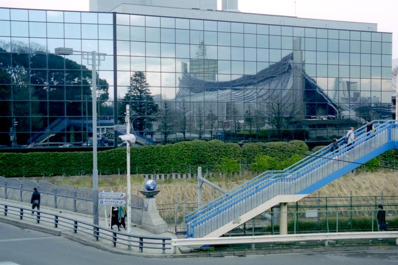 Le gymnase national Yoyogi se reflète dans la façade de verre d'un édifice.