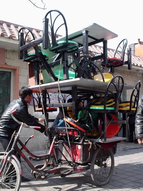 Un homme charge des tables de restaurant sur un tricycle.